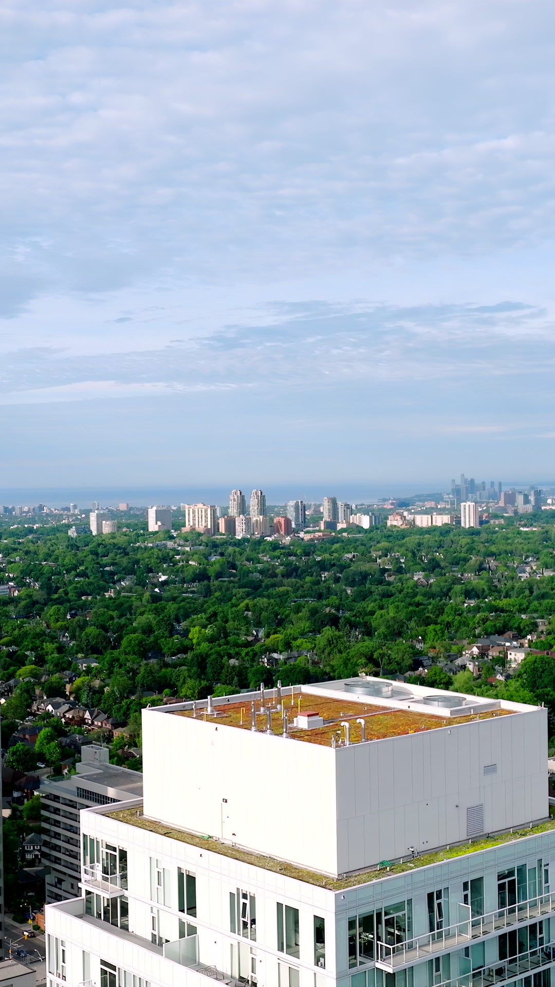 Aerial View of Modern White Condo Building with Green Roof and City Skyline — Premium 4K stock footage