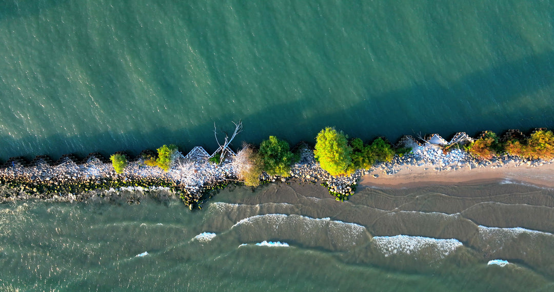 Aerial Drone View of Turquoise Waves Breaking on Rocky Shoreline with Autumn Trees — Premium 4K stock footage