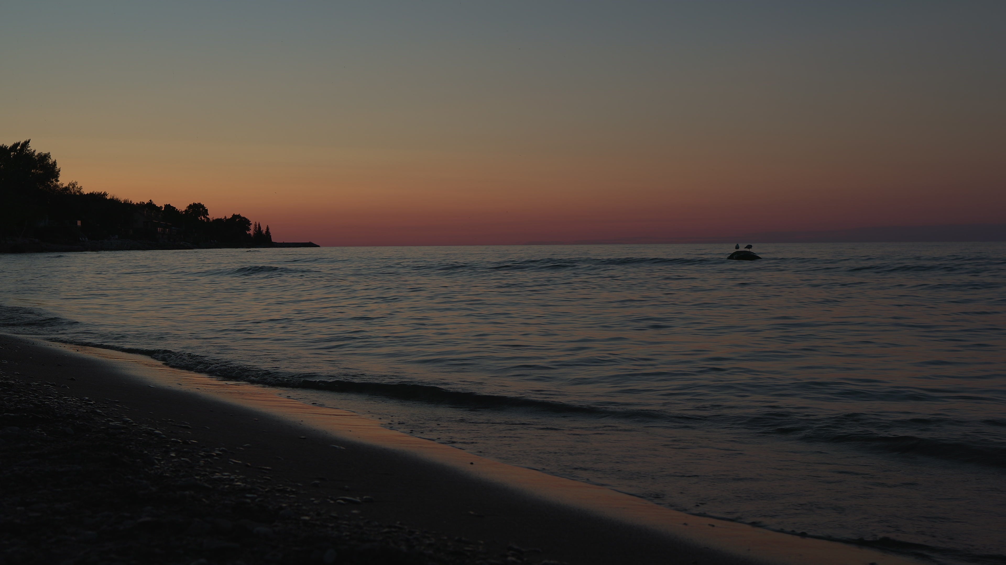 Serene Beach Sunset with Gentle Waves and Silhouetted Shoreline in Canada — 4K stock footage