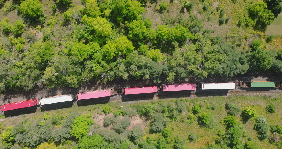 Aerial Top Down View of Colorful Freight Train Moving Through Lush Green Forest — Premium 4K stock footage